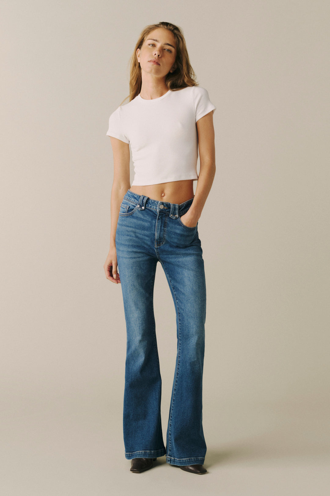 A woman modeling a pair of blue high-waisted flare jeans with a white cropped t-shirt.