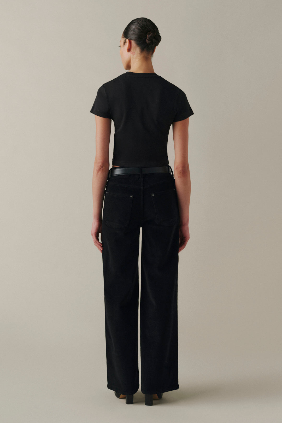 A model shown from the back wearing a black short-sleeve crop top and black wide-leg trousers.