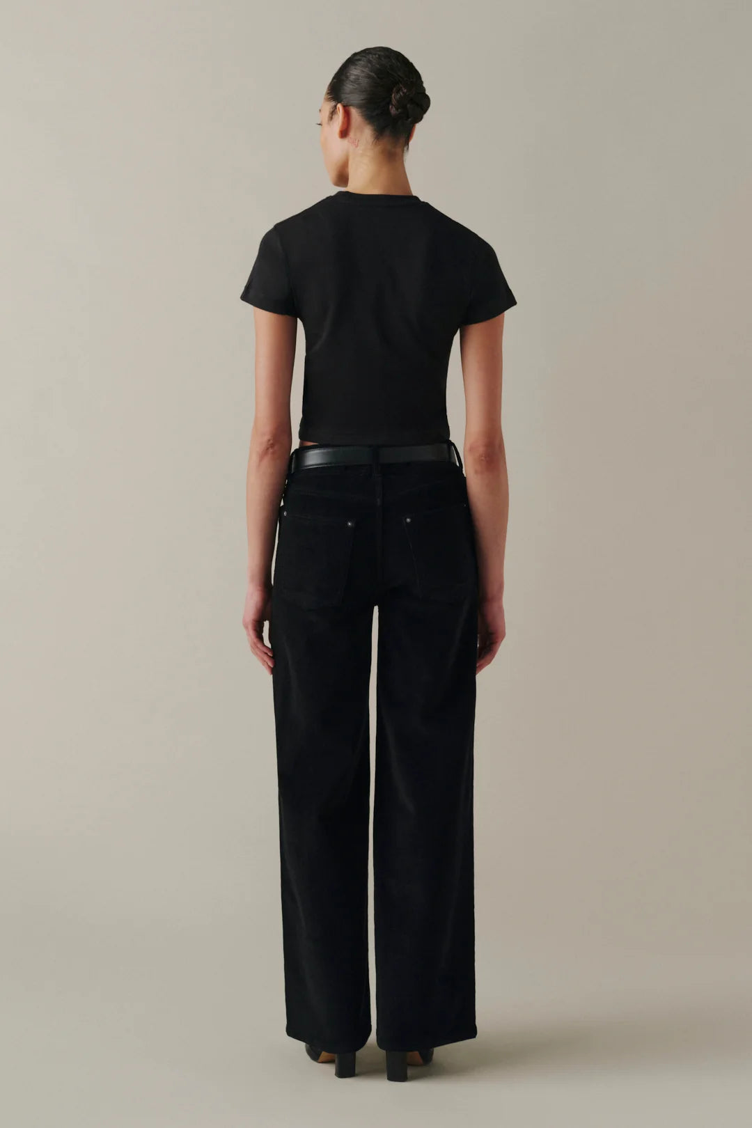 A model shown from the back wearing a black short-sleeve crop top and black wide-leg trousers.