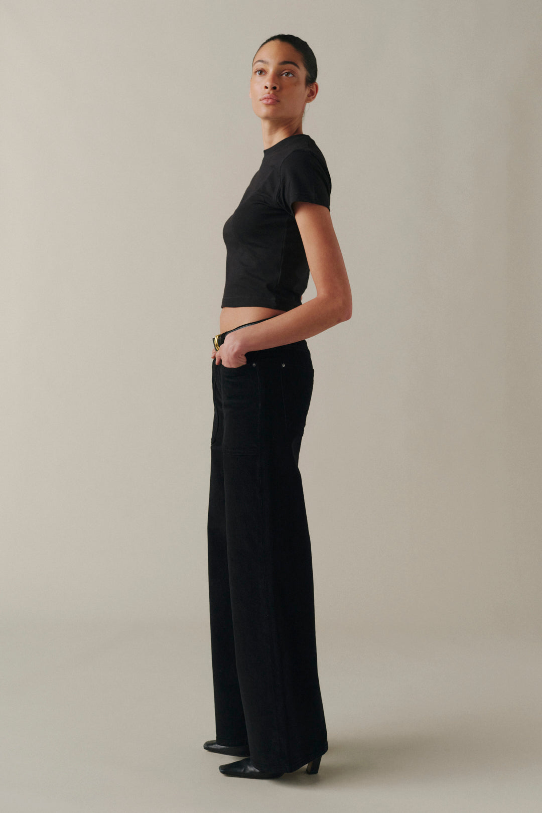 A model stands in profile wearing a black short-sleeve cropped top and black wide-leg trousers.