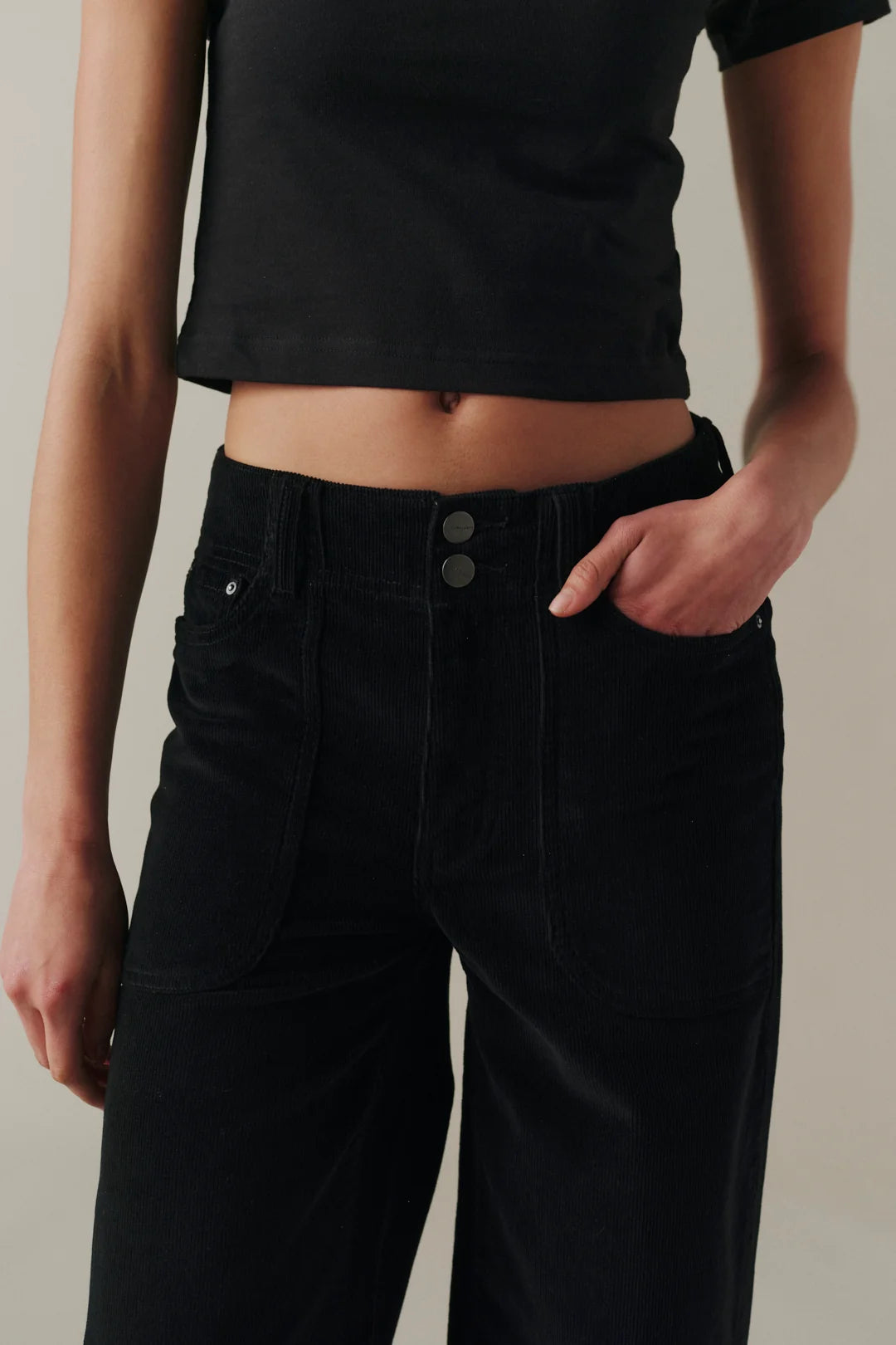 Close-up of a person wearing black corduroy pants with a button fly and a black cropped top.