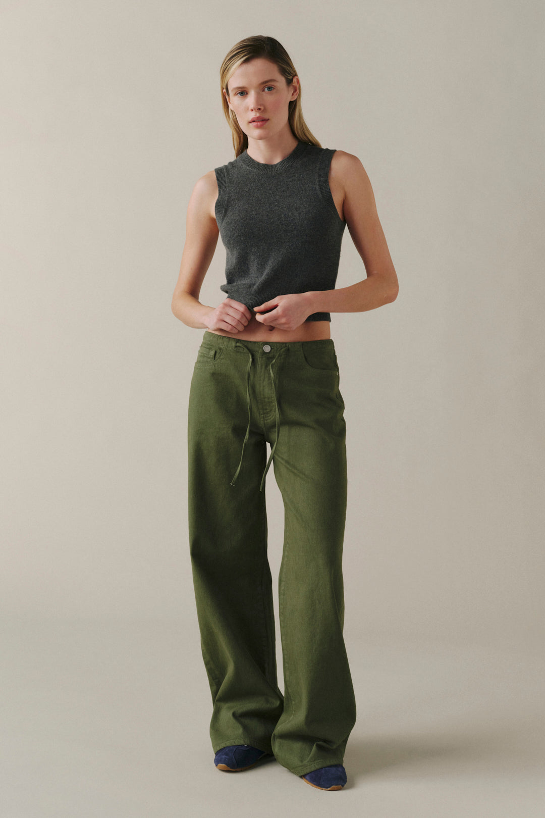 A woman modeling a dark gray ribbed sleeveless crop top and olive green wide-leg pants against a plain beige studio background.