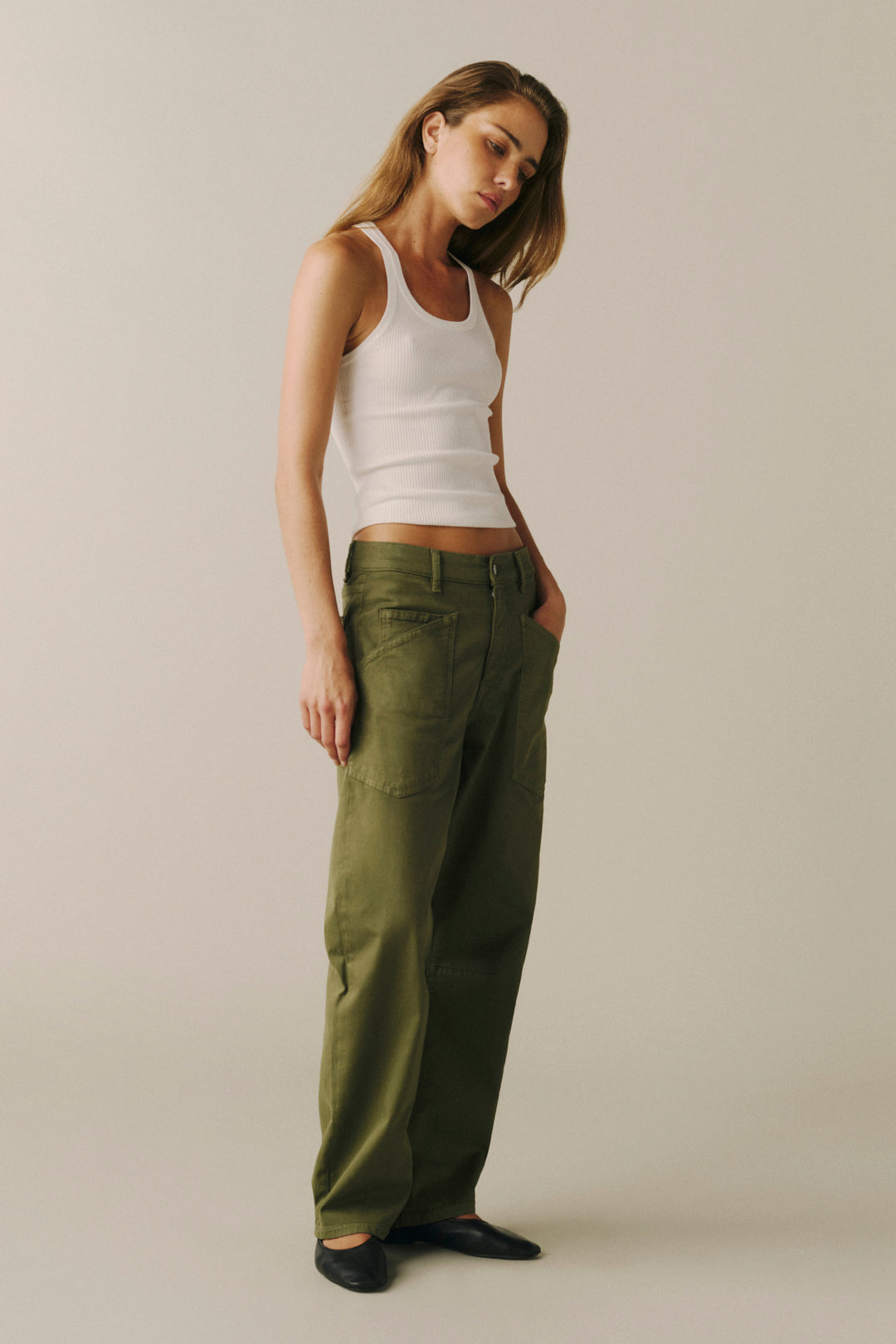 A woman modeling a pair of relaxed-fit olive green pants with a white ribbed tank top.