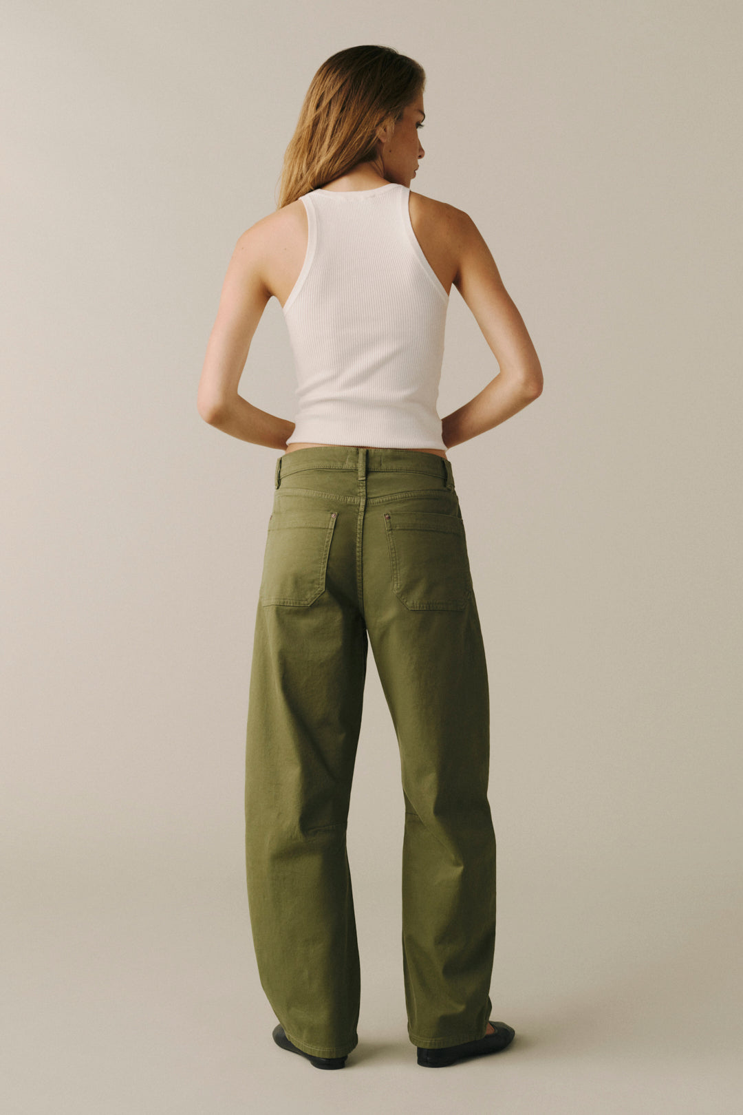 A woman shown from the back wearing olive green wide-leg pants and a white ribbed tank top.