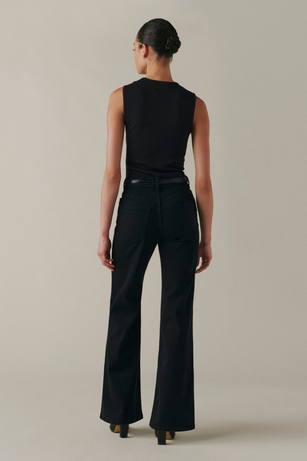 A model shown from the back wearing a black sleeveless top and black wide-leg pants against a neutral beige studio background.