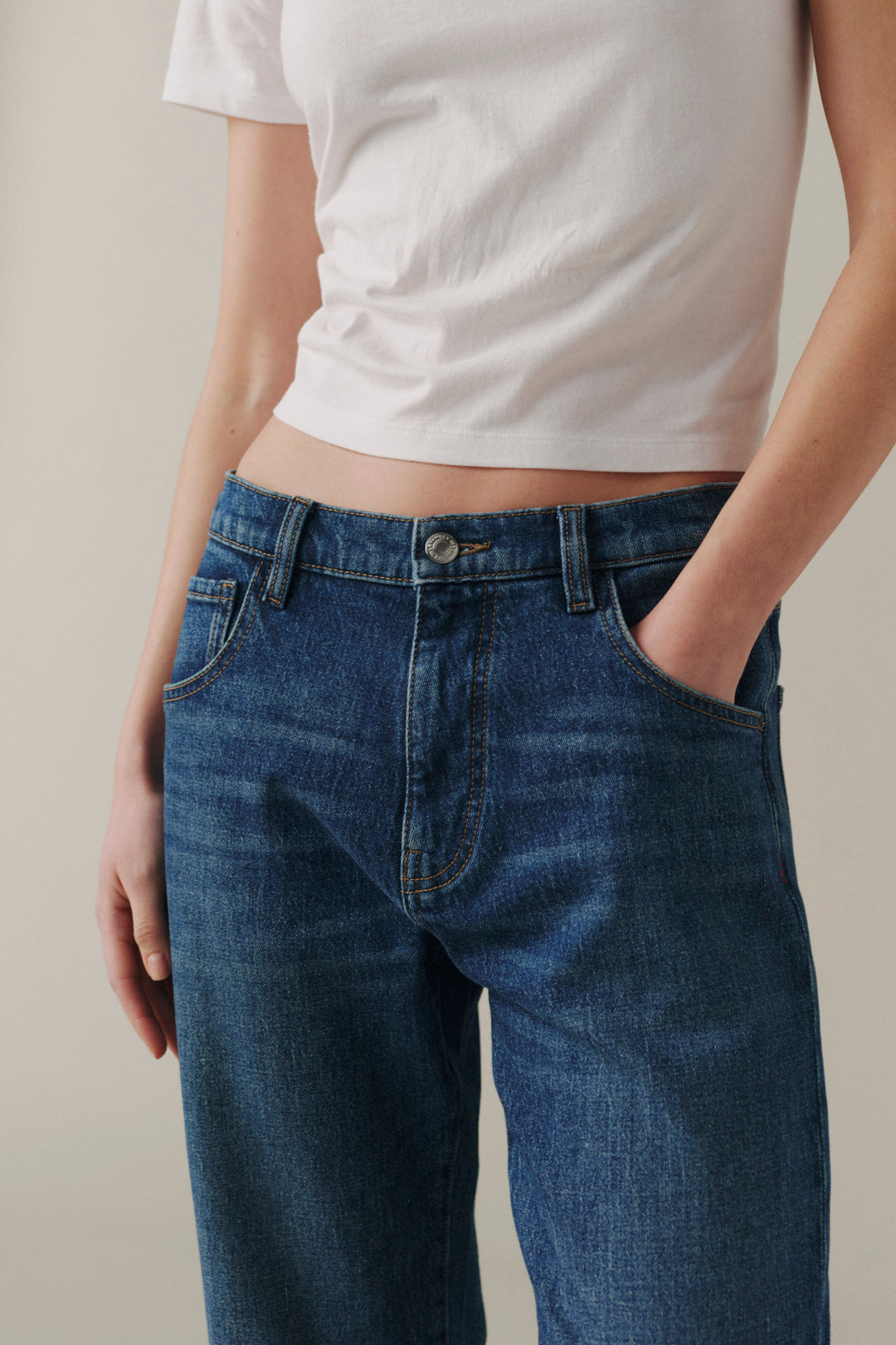 A close-up of a person wearing dark blue denim jeans and a white cropped T-shirt.