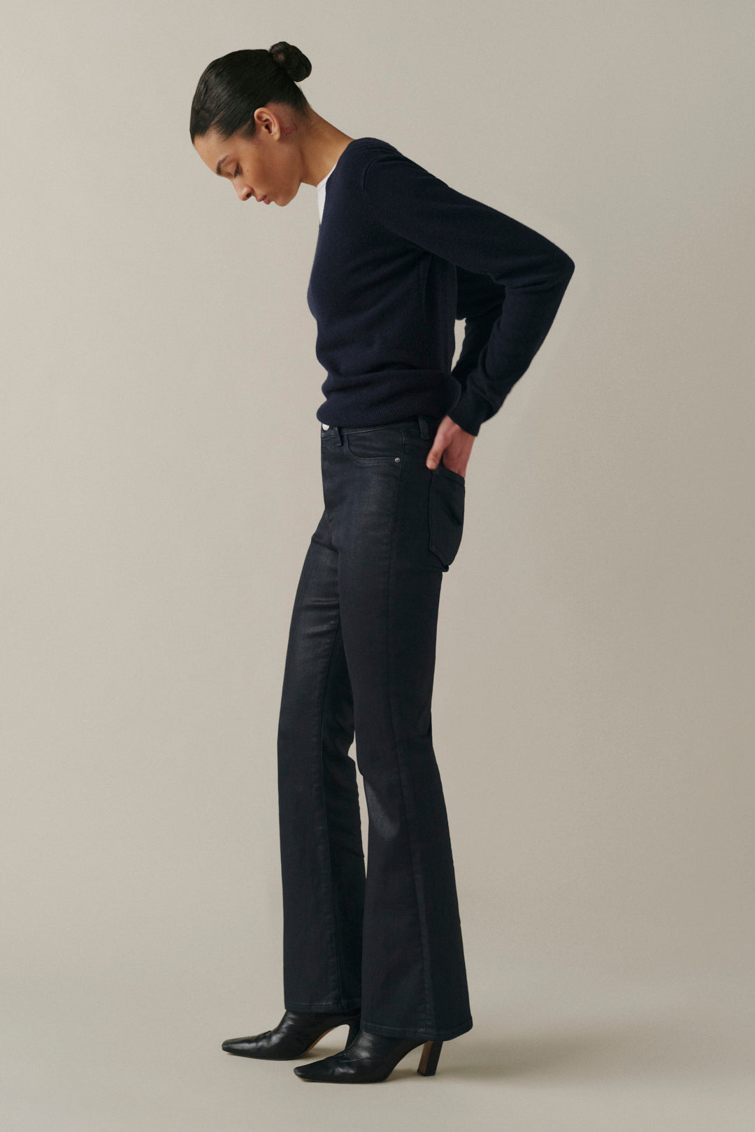 A woman modeling dark navy blue wide-leg trousers with a subtle textured sheen, paired with a matching dark sweater and black ankle boots, set against a solid light beige studio background.