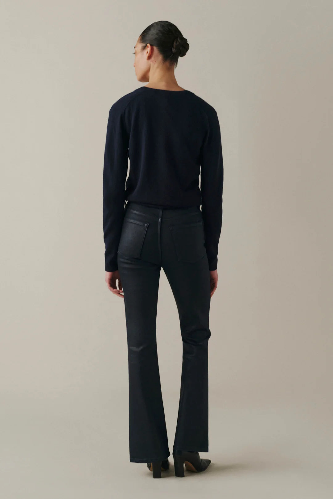 A model shown from the back wearing a dark navy long-sleeve top and matching dark navy flared pants against a solid light beige studio background.