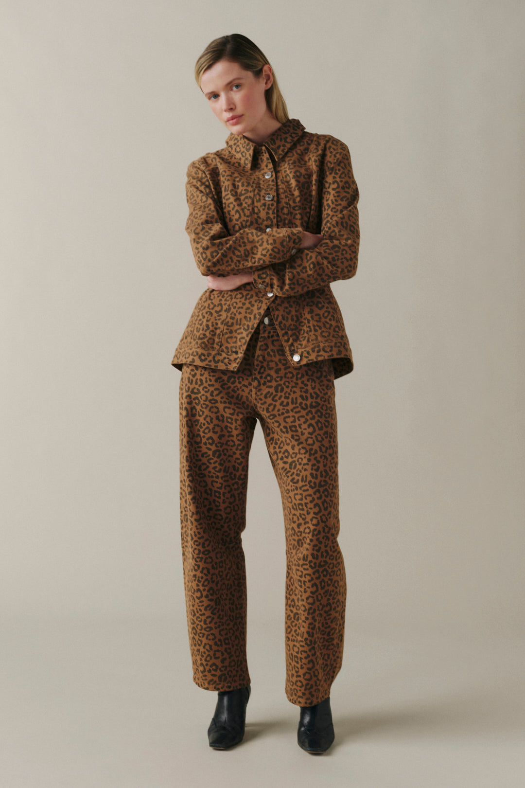 A model wearing a matching brown and black leopard-print jacket and trousers set, paired with black boots.