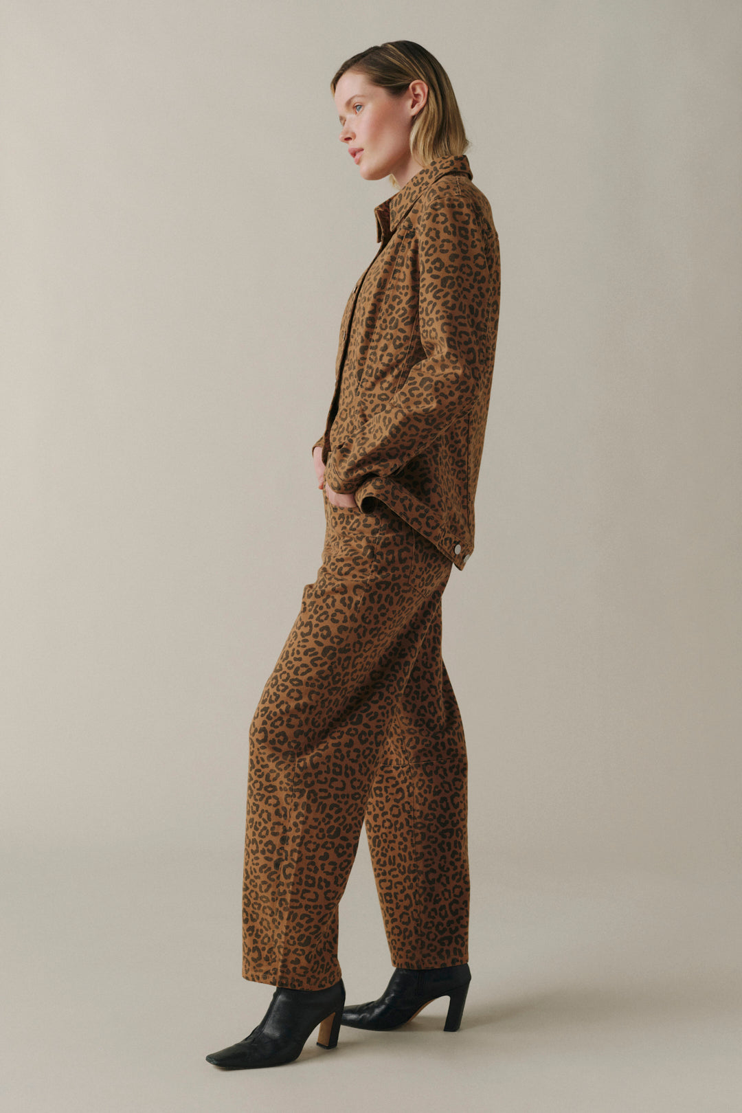 A woman stands in profile wearing a brown and black leopard-print blazer and matching wide-leg trousers.