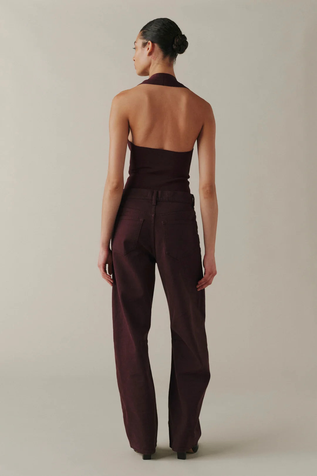 A model shown from the back wearing a dark plum-brown halter top and matching wide-leg trousers against a plain light beige studio background.