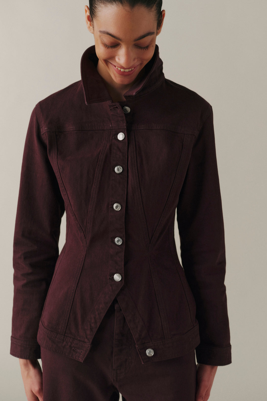 A woman wearing a dark plum-colored jacket with a high collar and silver buttons, paired with matching dark pants.