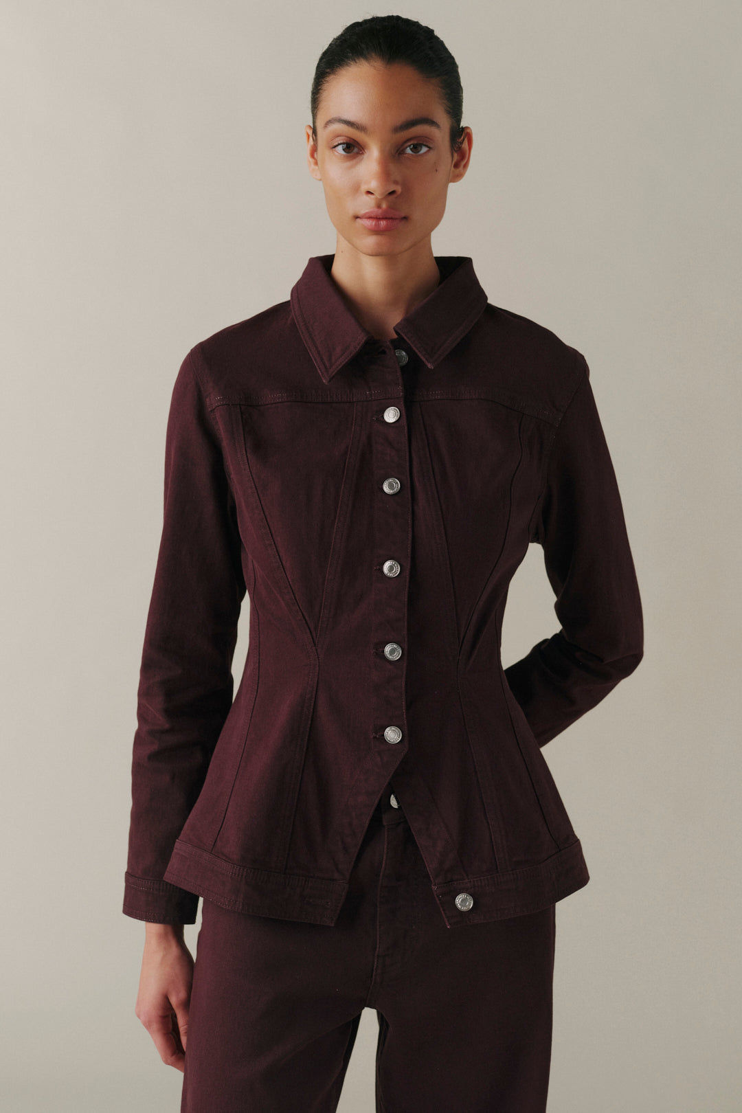 A model wearing a dark burgundy button-up jacket with structured shoulders and matching trousers.