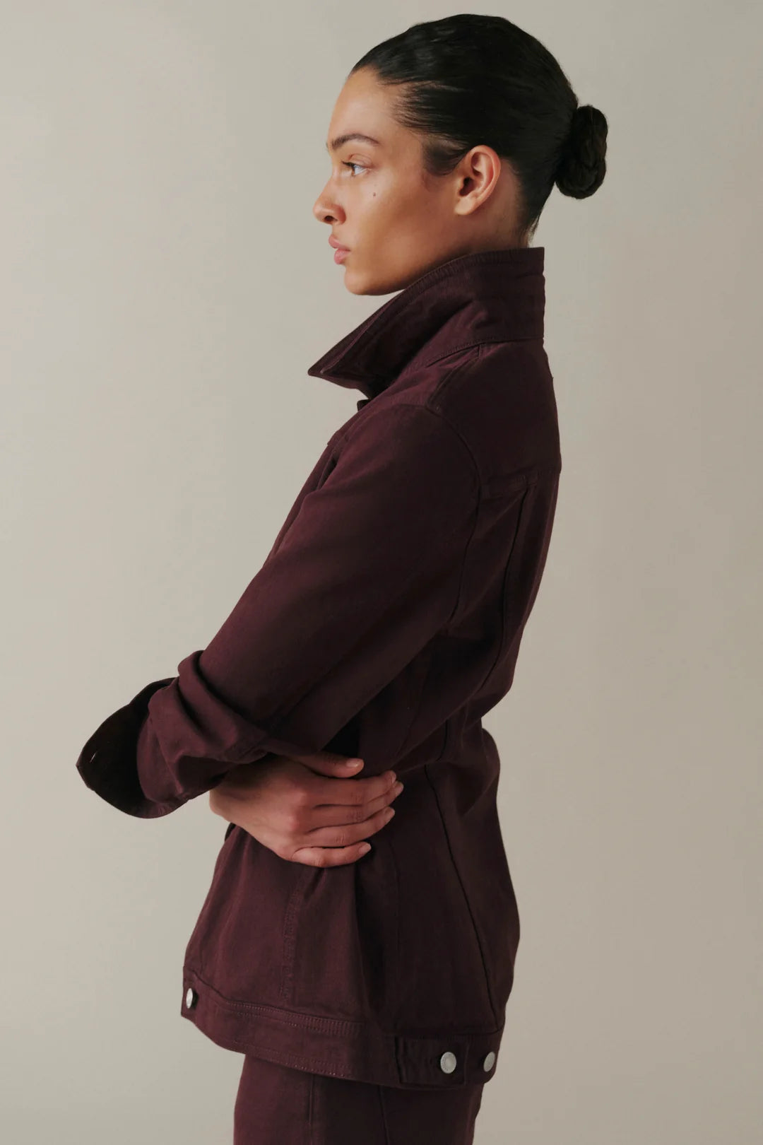 A woman in profile wearing a dark plum-burgundy utility jacket with a high collar and matching pants.