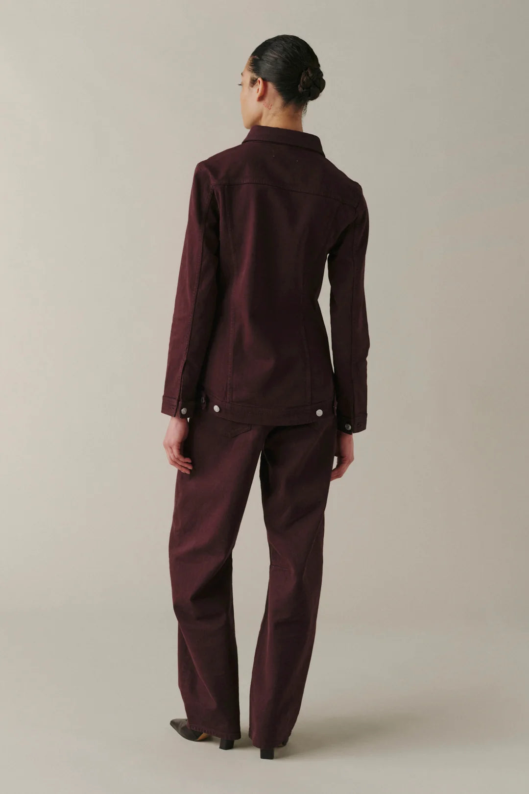 A model viewed from the back wearing a matching dark burgundy button-up shirt and trousers set.