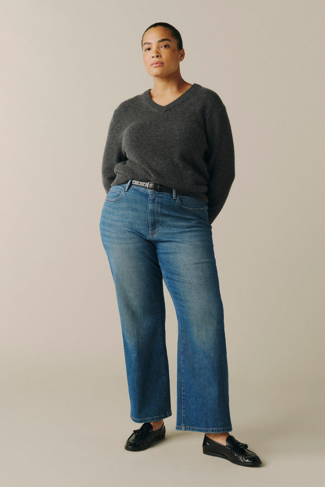 A model wearing a dark gray v-neck sweater, blue wide-leg jeans, and black leather loafers.