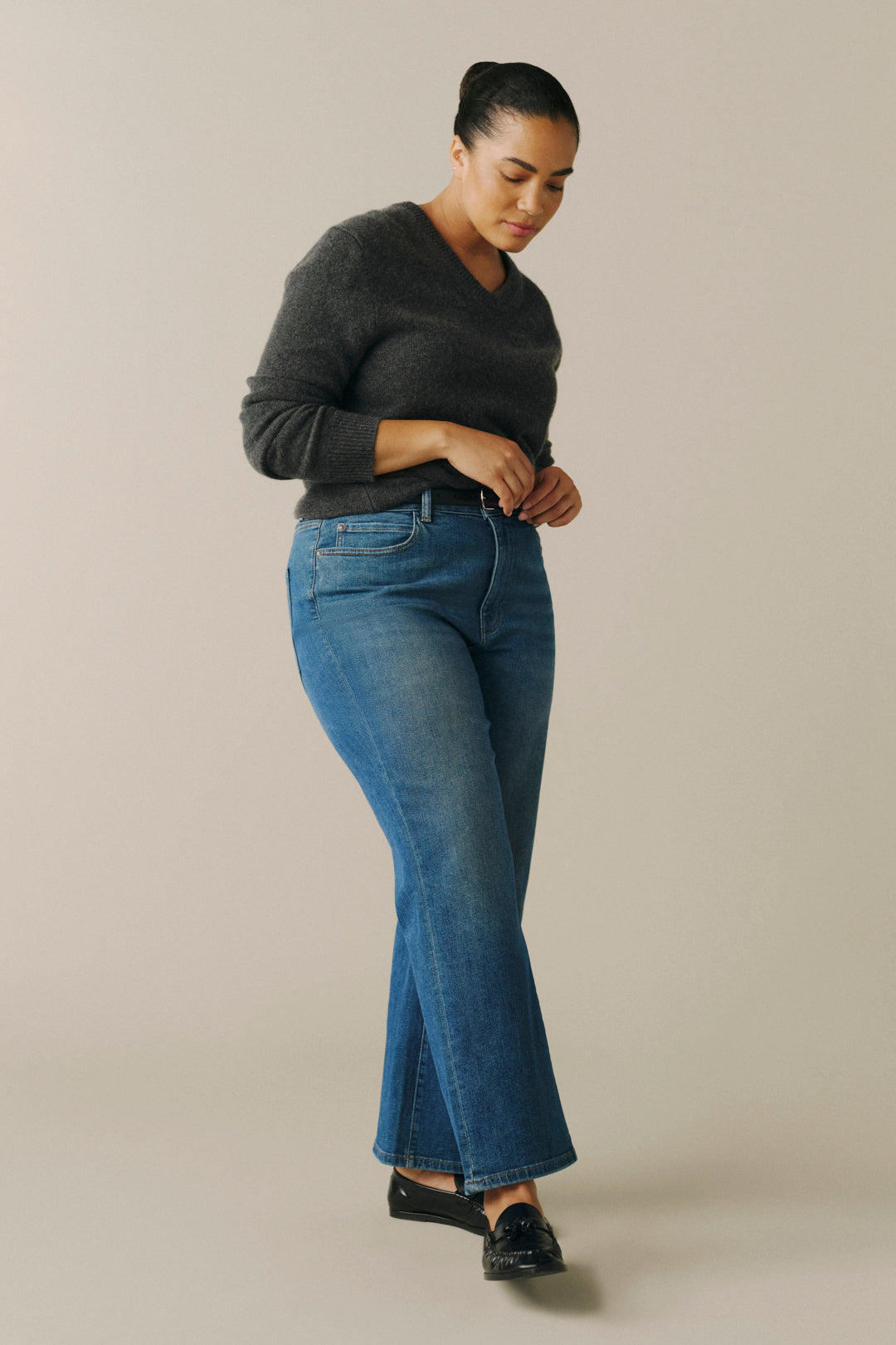 A woman modeling a pair of medium-wash blue flare jeans with a dark gray long-sleeve sweater and black loafers.