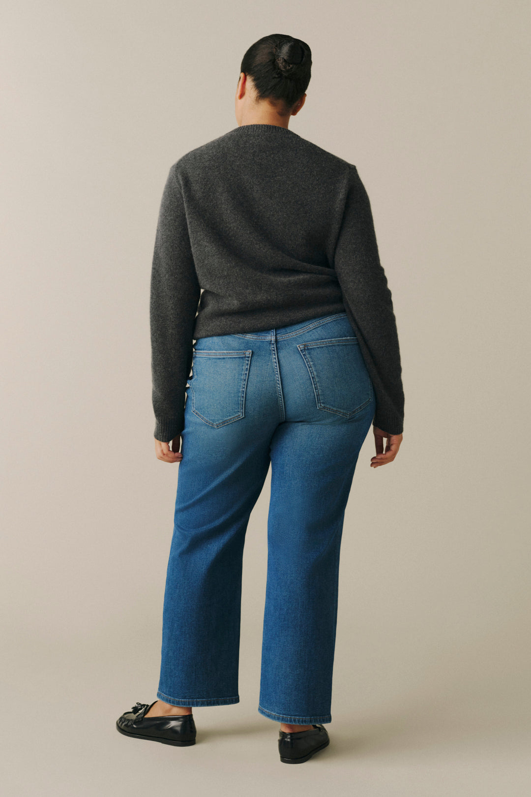 A person shown from the back wearing a dark charcoal gray sweater and blue wide-leg jeans.