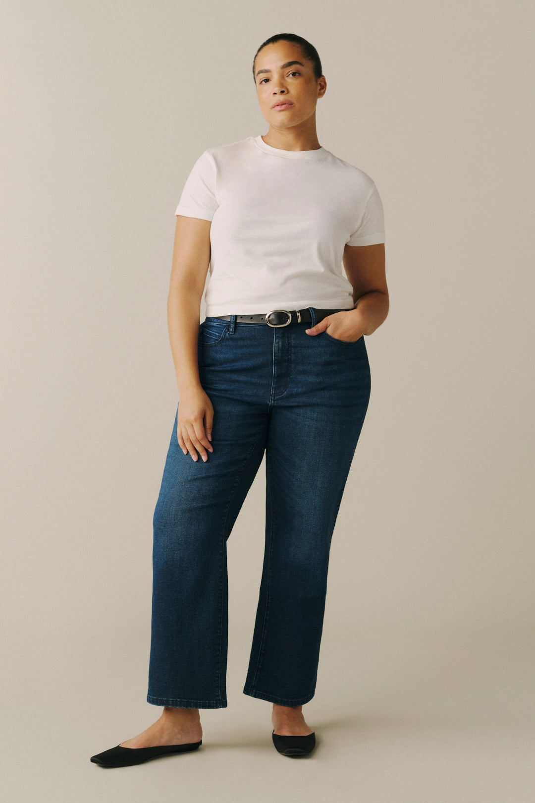 A model wearing dark blue wide-leg cropped jeans, a white t-shirt, and black flats.