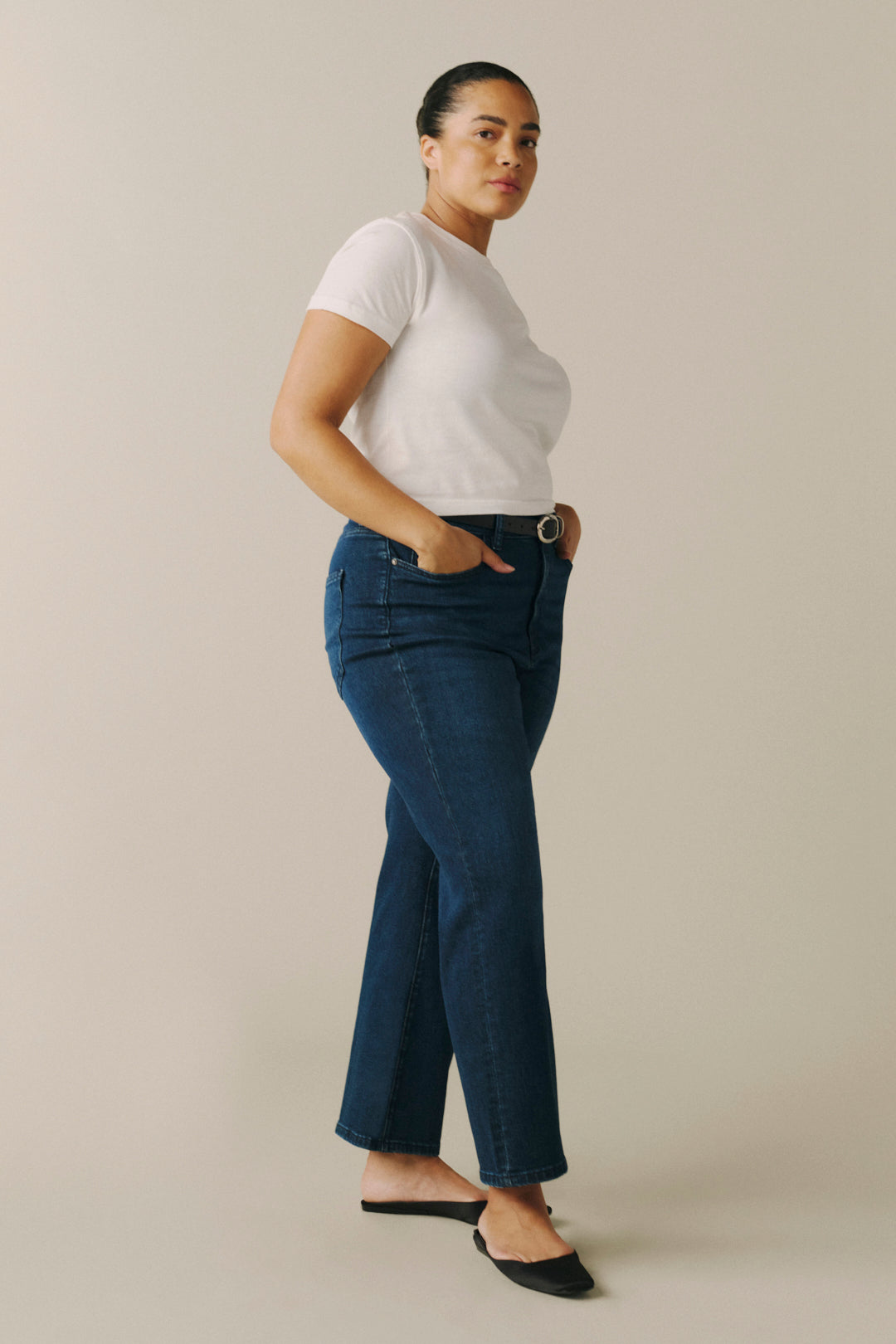 A woman modeling dark blue straight-leg jeans with a white t-shirt and black flat shoes.