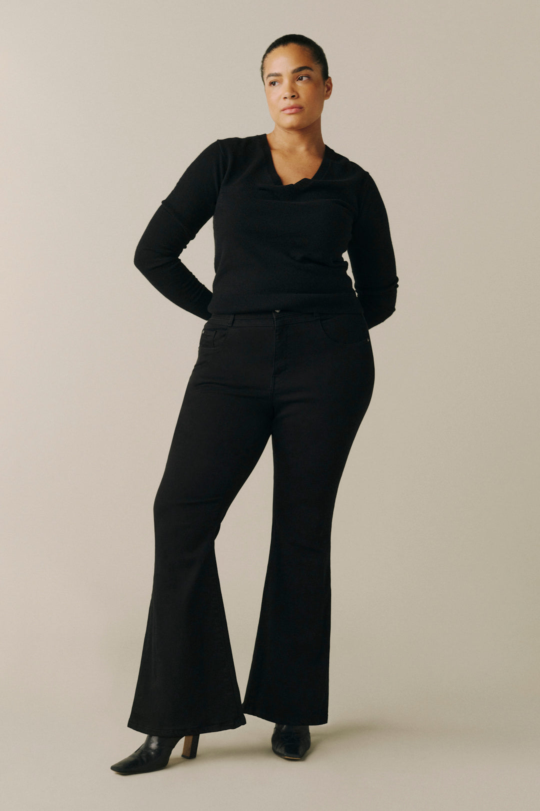 A woman modeling a black long-sleeve collared top and matching black flared pants.