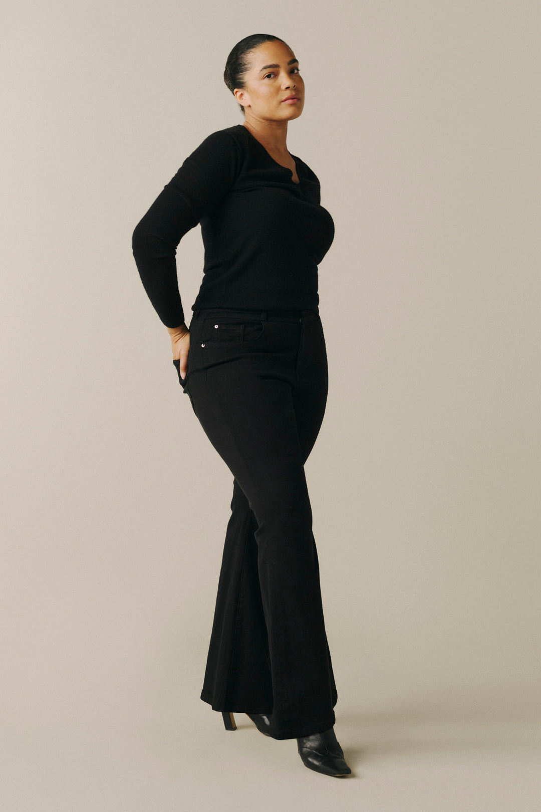 A woman modeling a black long-sleeve top and matching black flared pants against a plain beige studio background.