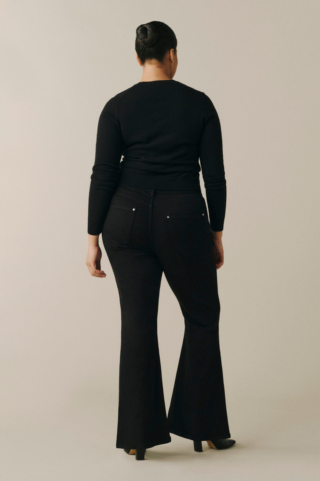 A woman viewed from the back wearing a black long-sleeve top and black flared pants.