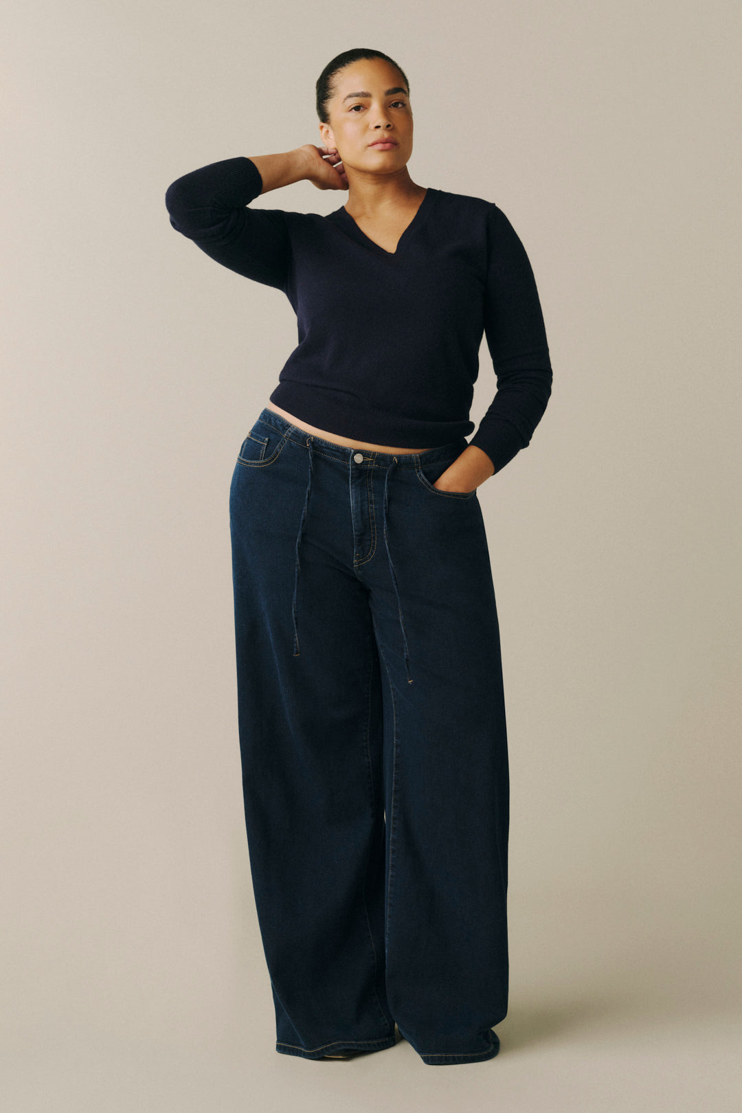 A model wearing a dark navy long-sleeve V-neck top and dark wide-leg denim jeans.