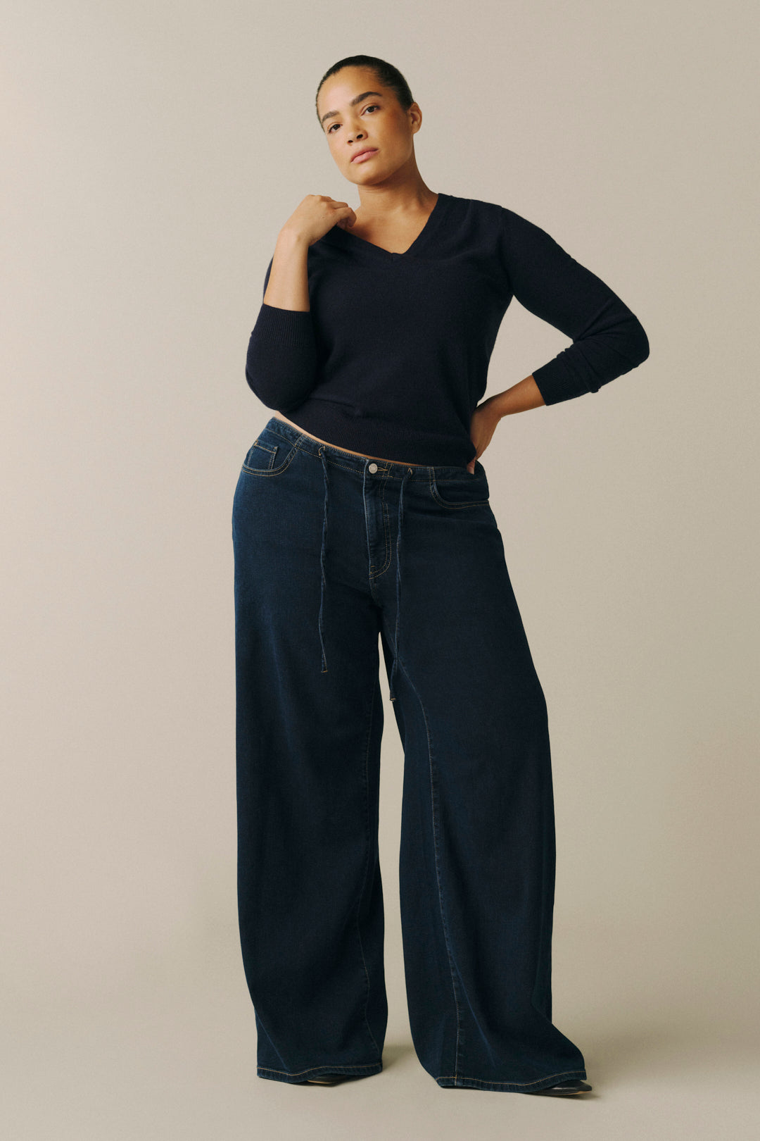 A model wearing a black long-sleeve V-neck top and dark wide-leg denim jeans.