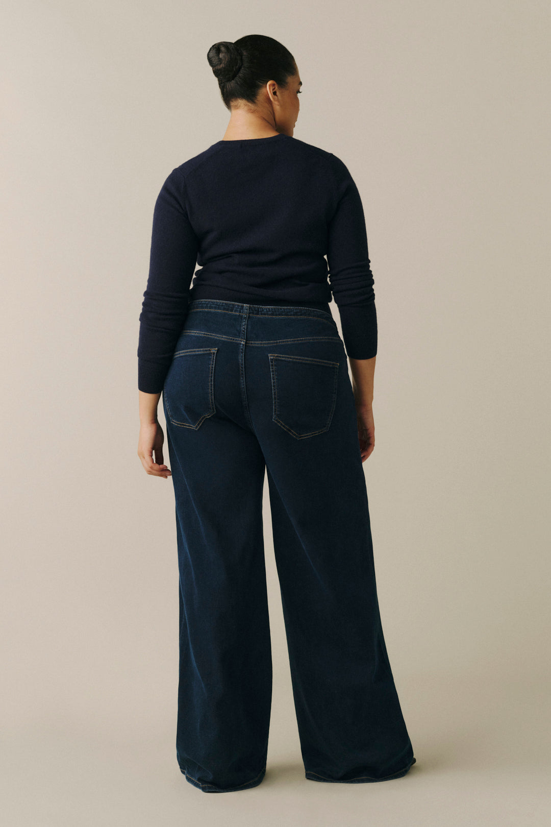 A woman viewed from the back wearing a dark navy long-sleeve top and dark blue wide-leg jeans.