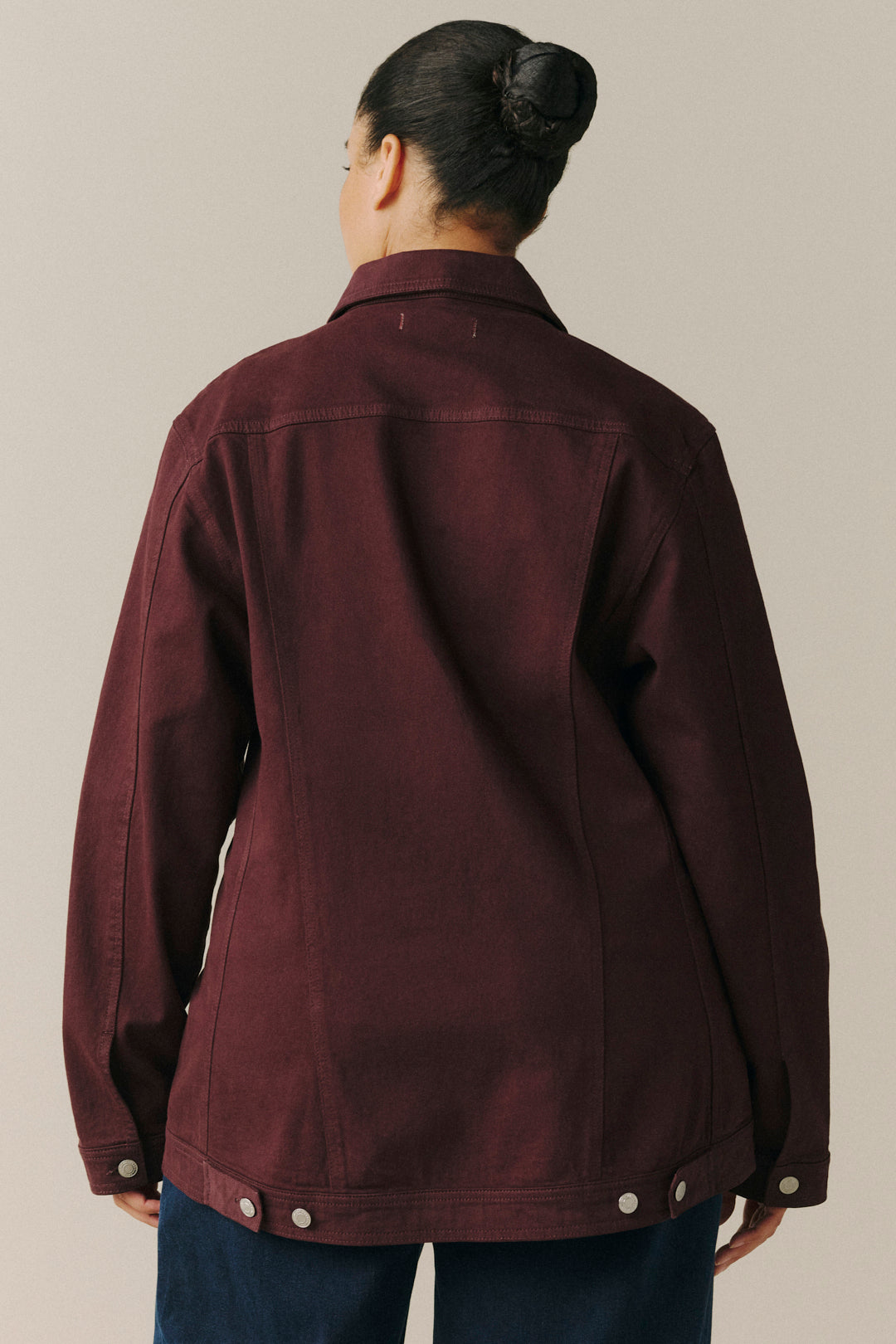 A person shown from the back wearing a dark burgundy utility jacket with snap-button details at the cuffs and hem.
