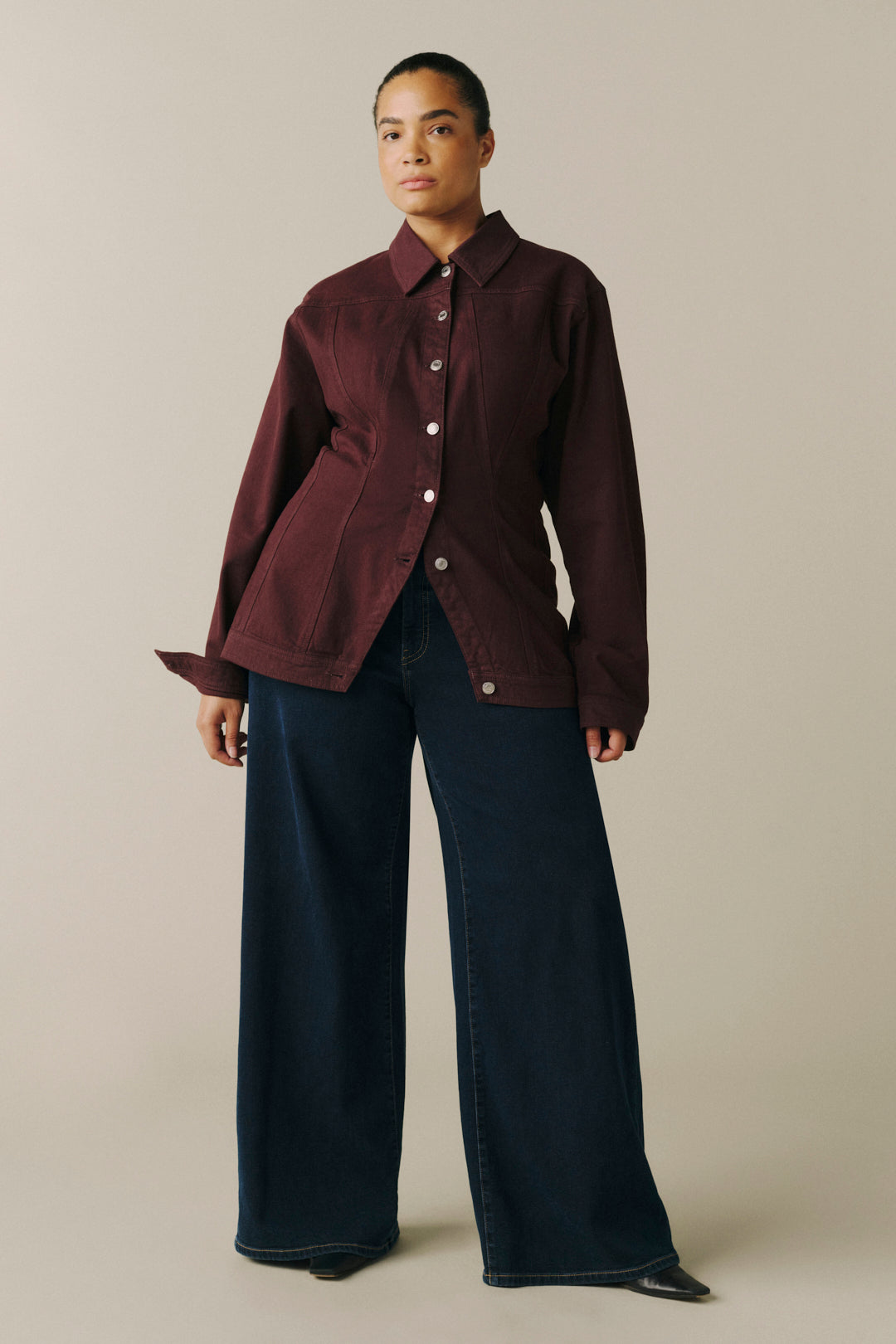 A model wearing a dark burgundy button-up shirt jacket and dark wide-leg jeans.