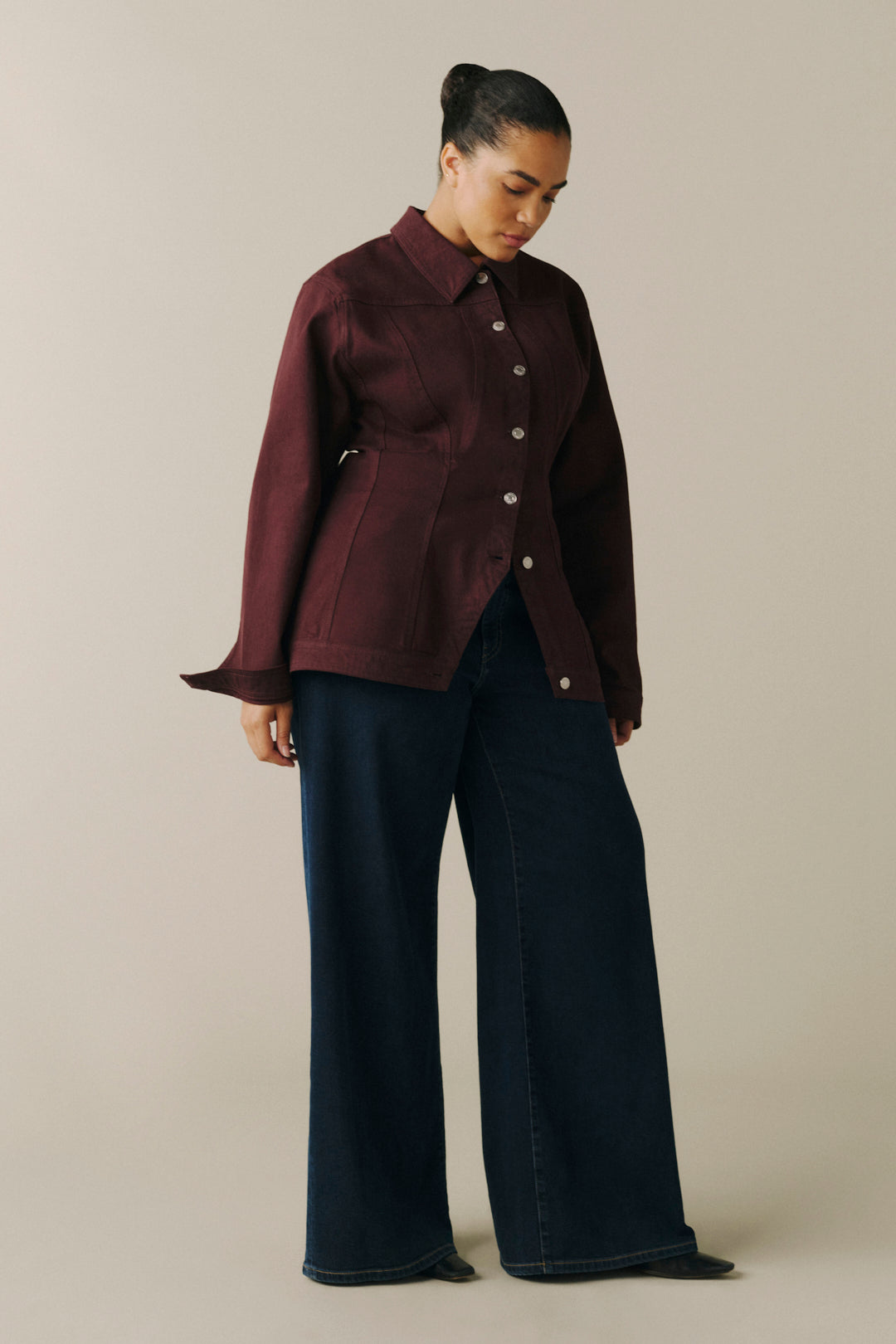 A model wearing a dark burgundy cropped button-up shirt jacket with wide cuffs and dark navy wide-leg jeans.