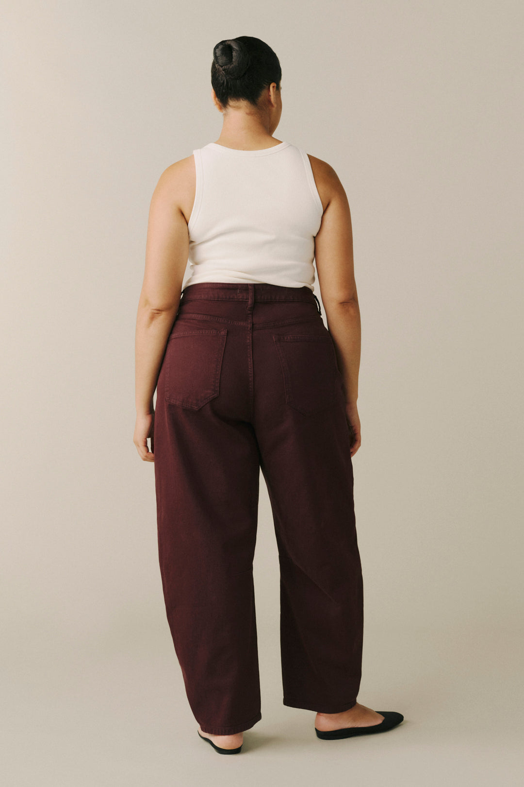 A model shown from the back wearing wide-leg burgundy trousers, a white sleeveless top, and black flats.