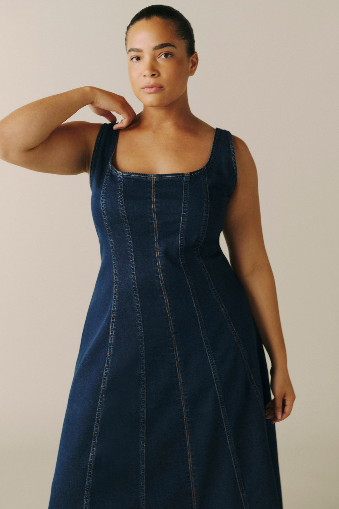 A woman modeling a dark blue denim midi dress with a square neckline and vertical seam details.