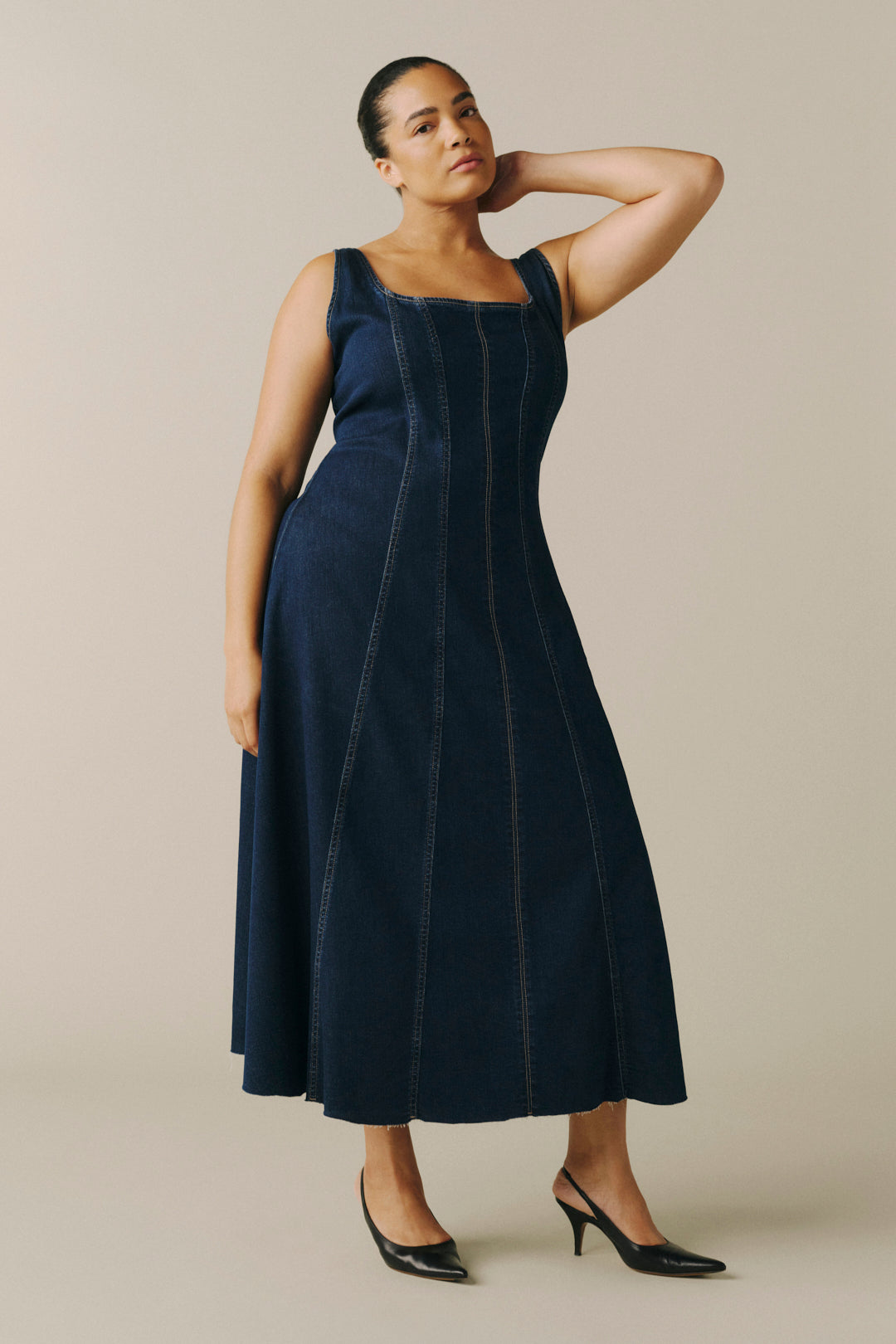 A woman modeling a sleeveless dark navy midi dress with vertical seam detailing, styled with black pointed-toe heels.