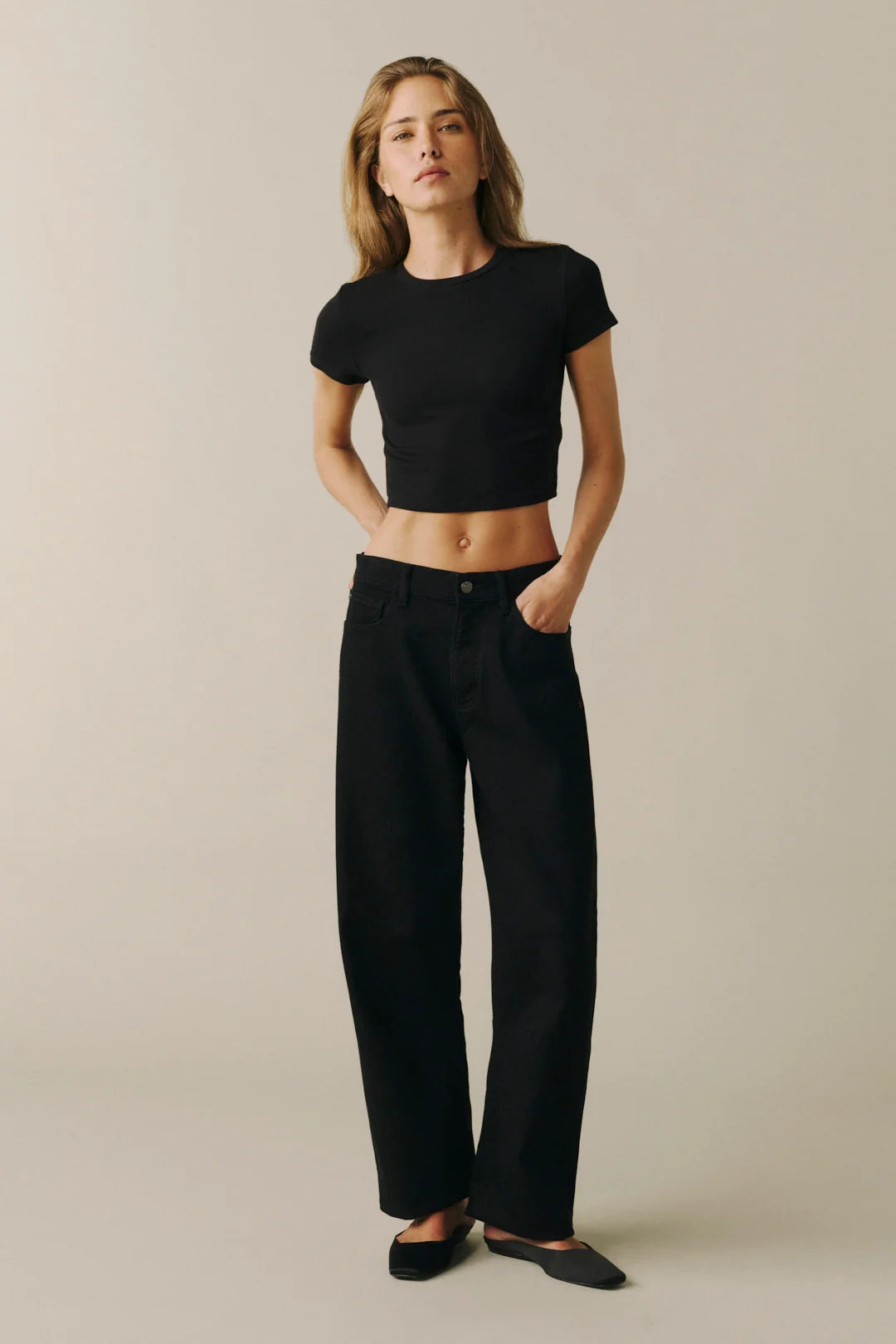 A woman modeling a black short-sleeve crop top and black wide-leg pants against a plain beige studio background.