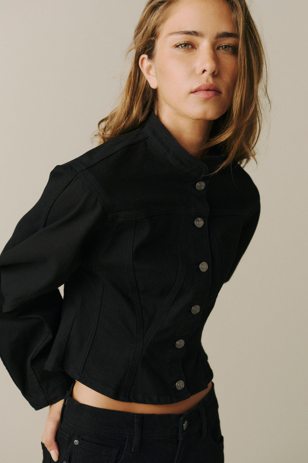 A woman wearing a black cropped jacket with a high stand collar and front buttons, paired with black jeans.