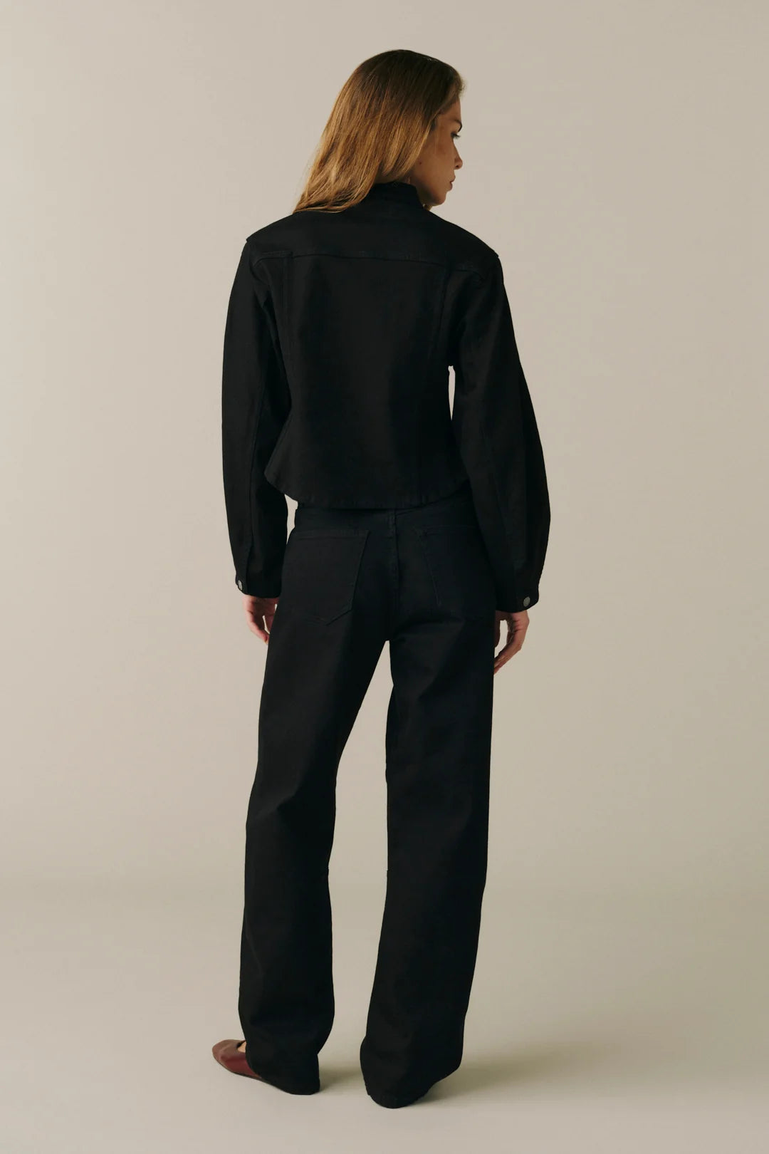 A model is shown from the back wearing a black cropped jacket and matching black wide-leg trousers.